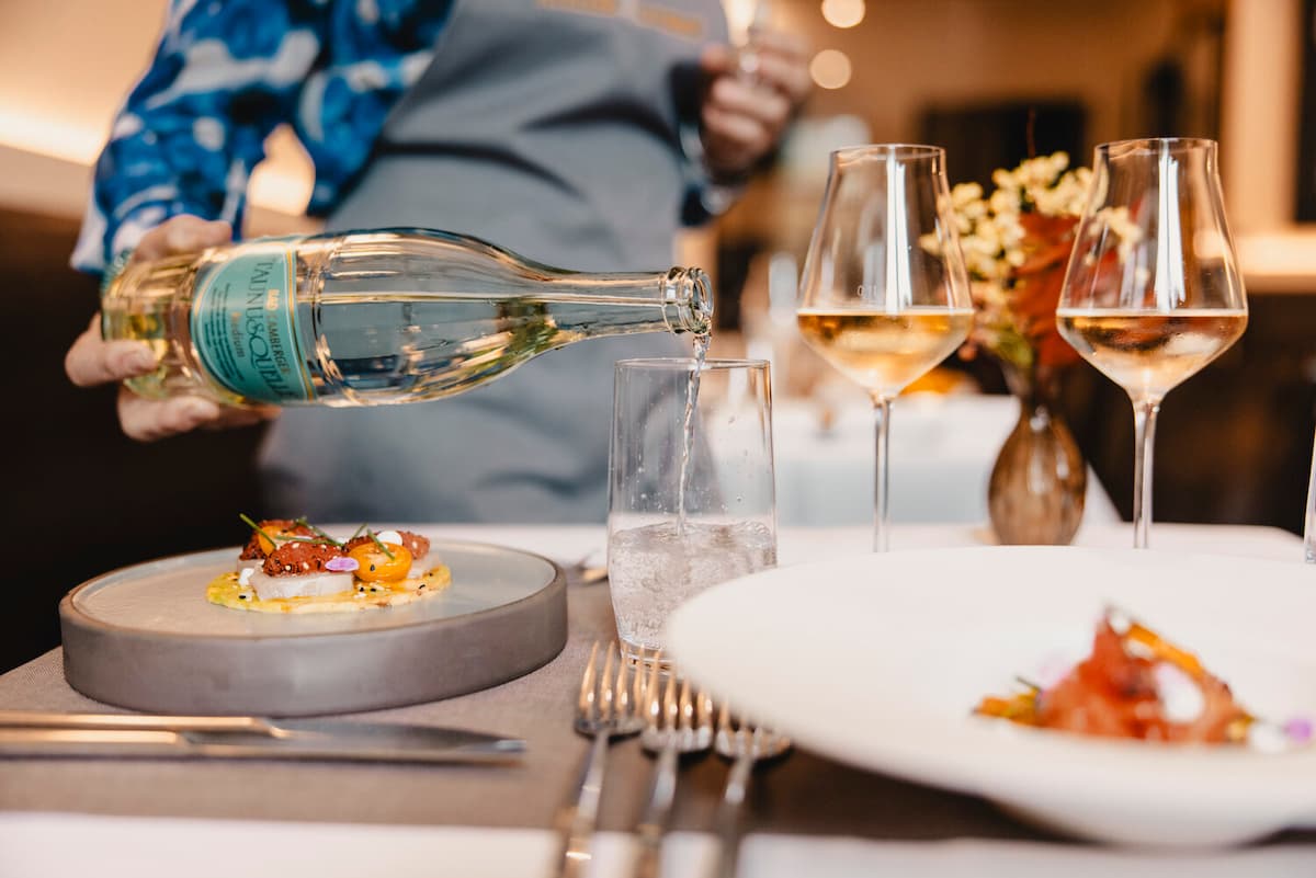 Water cascades into a glass as elegant appetizers await—a refined dining moment captured with golden light and artistic plating.