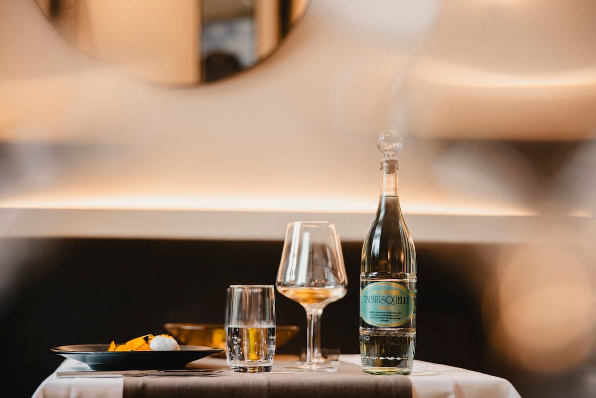 Elegant table setting: Tauni&Quell water bottle with crystal glasses and gourmet dessert in warm, softly lit dining space.