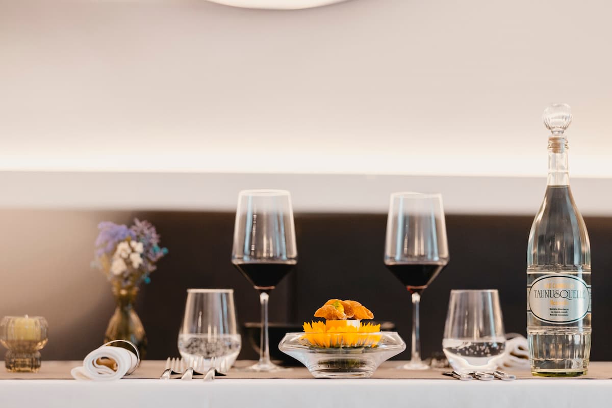 A refined restaurant table set with wine glasses, water, and a dish adorned with bright yellow petals, lit softly against a minimalist background with a small vase of flowers.